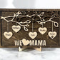 A wooden family hearts sign with multiple hanging hearts, each engraved with a name, and the phrase 'WE love MAMA' on a shiplap background with a dark walnut stained back.