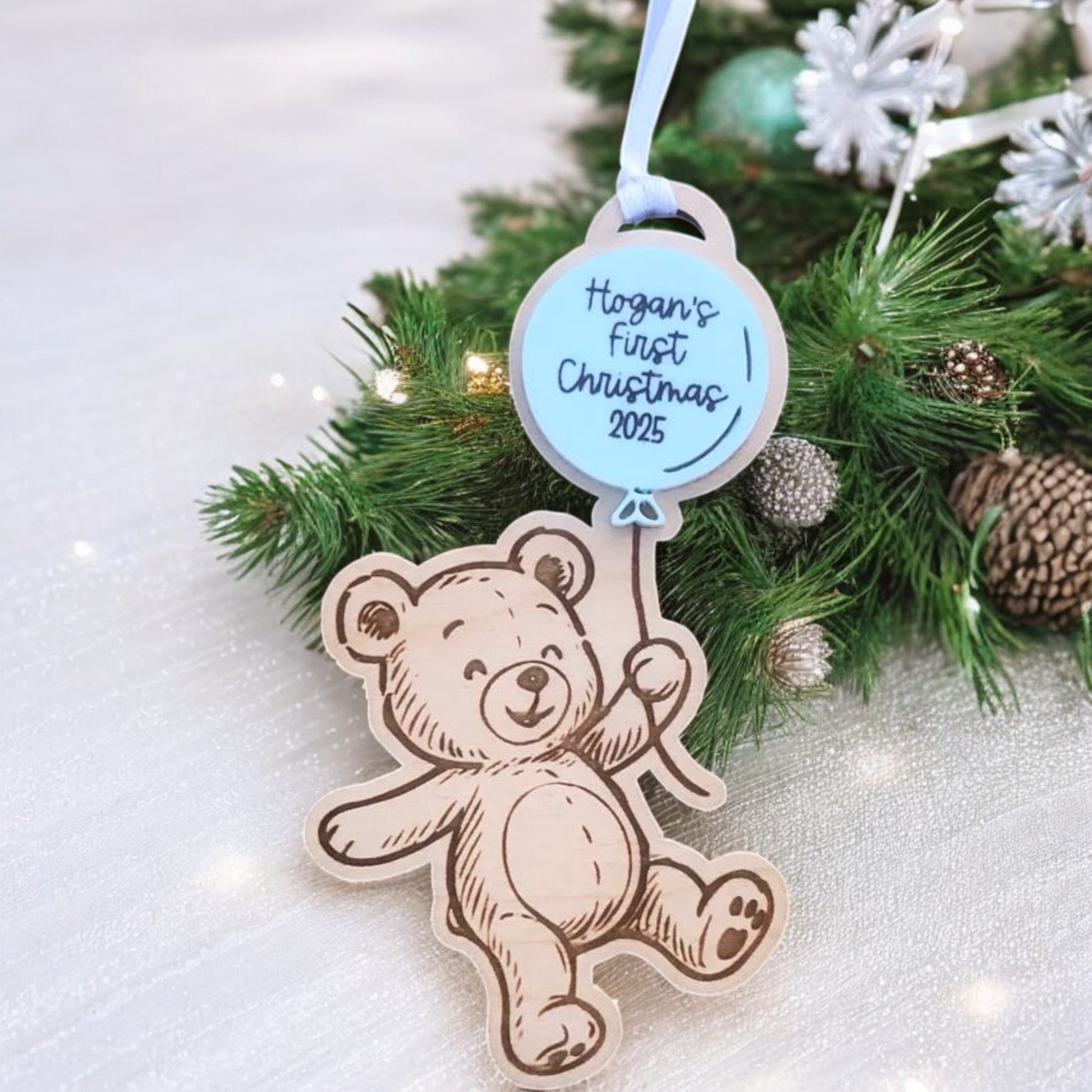 Decorative ornament with teddy bear design and 'Hogan's First Christmas 2025' text on a Christmas tree.