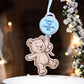 Decorative ornament with teddy bear design and 'Hogan's First Christmas 2025' tag, set against a festive background.