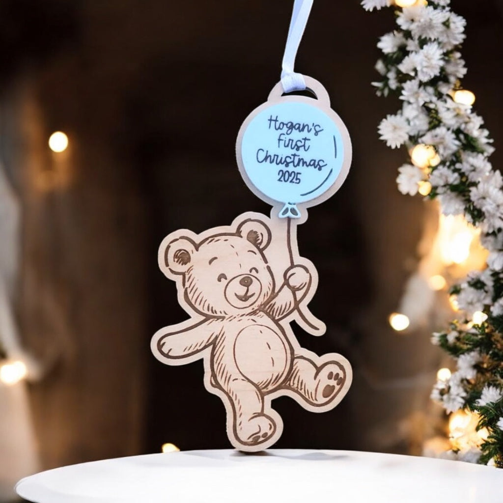 Decorative ornament with teddy bear design and 'Hogan's First Christmas 2025' tag, set against a festive background.